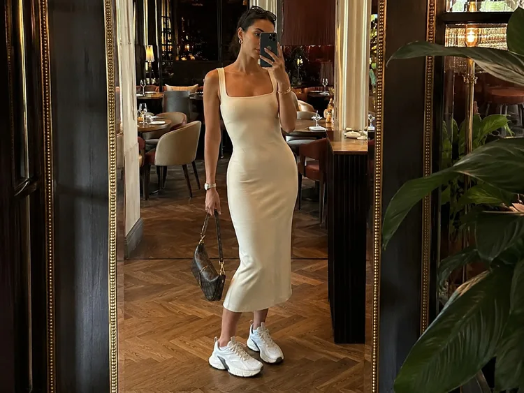 Mulher usando vestido midi claro com tênis feminino branco da Pegada em look athleisure para o fim de semana, em ambiente de restaurante.